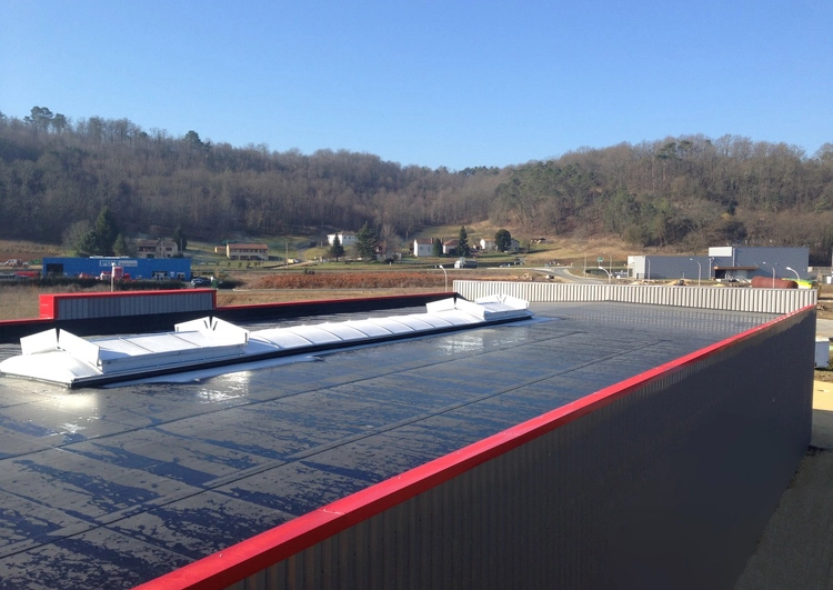 bâtiment industriel en tôle couvert en membrane EPDM, à l'arrière plan une zone industriel et des collines boisées.