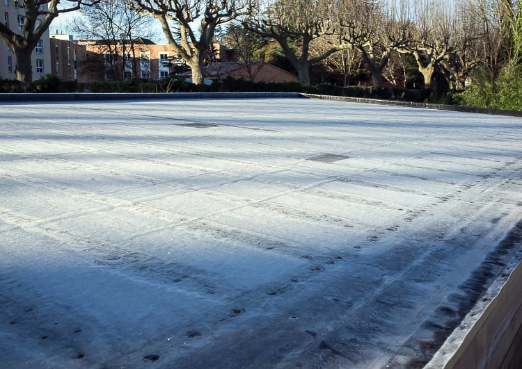 grande toiture plate couverte en membrane EPDM, la surface est givré et ensoleillée, à l'arrière plan des arbres et des bâtiments résidentiels