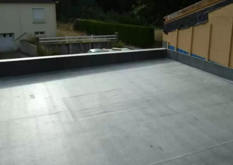 au premier plan la toiture plate est couverte en membrane EPDM, sur le coté droite il y a un mur de la construction voisine, au fond il y a une maison