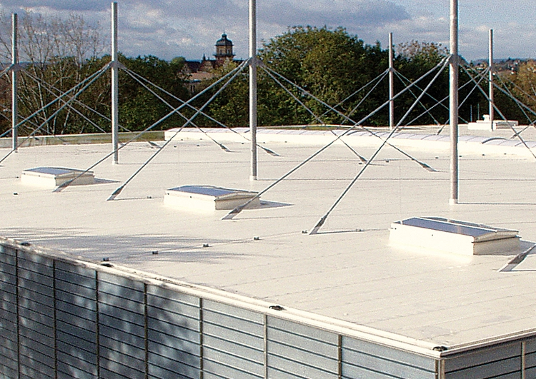 toiture plate couverte en membrane TPO blanche, à l'arrière plan le clocher d'une église dépasse de la végétation.