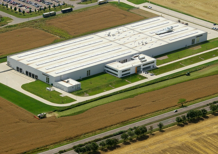 vue d'avion d'un grand bâtiment industriel entourée de champs, un parking et les routes d'accès.