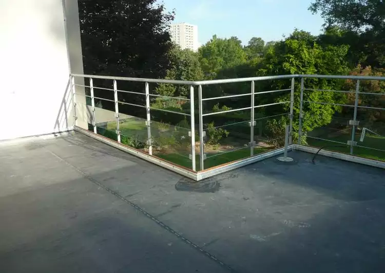 toit terrasse couvert en membrane EPDM bordé de barrières, à l'arrière-plan un jardin.