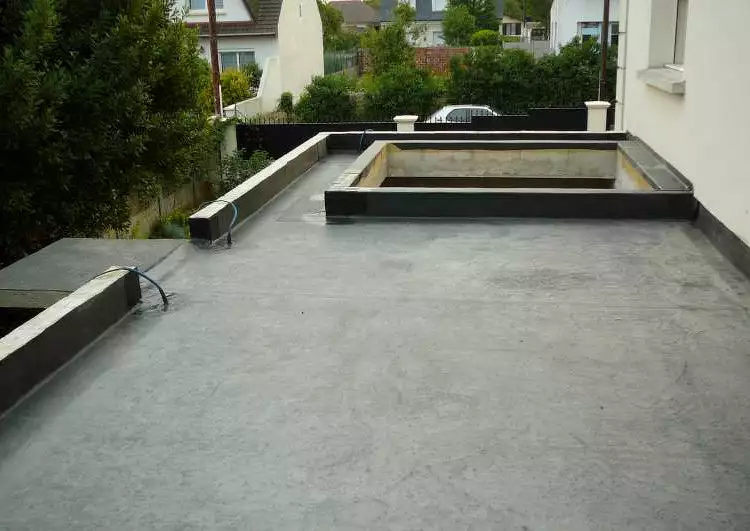 toiture plate couverte en membrane EPDM, bordée par des acrotères sauf à droite par un mur, une zone non couverte au milieu de la toiture est bordée d'accrotères aussi, l'arrière plan montre une zone résidentielle.