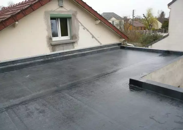 toit plat couvert en EPDM, temps pluvieux, sur la gauche un mur avec une fenêtre, sur la droite les acrotères, à l'arrière-plan on voit la construction voisine.