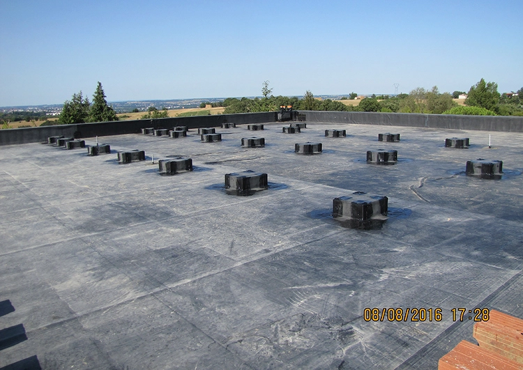 Au premier plan vaste toiture plate avec étanchéité en EPDM, à l'arrière plan paysage de plaine de Haute Garonne